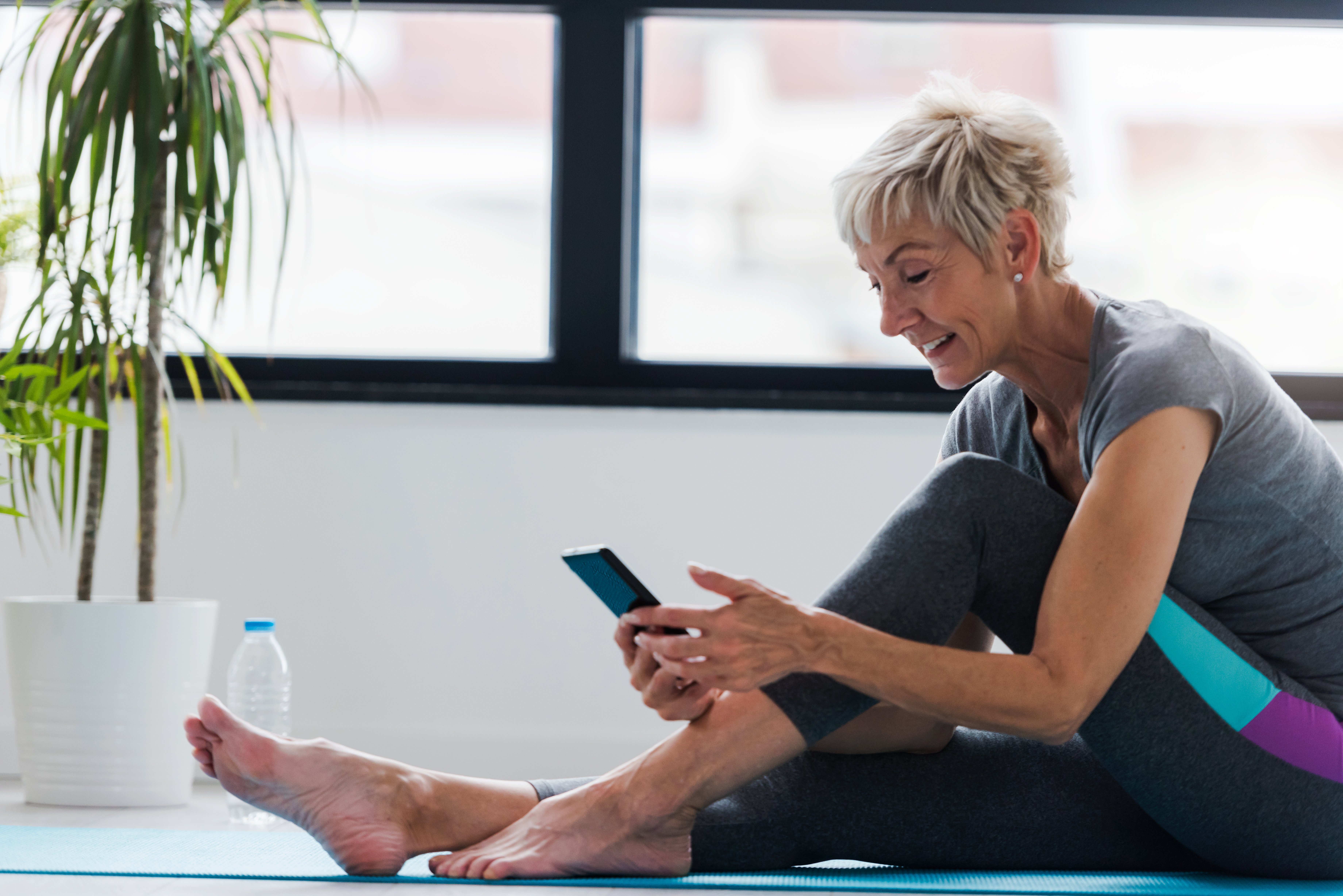 Woman using mobile phone on yoga mat